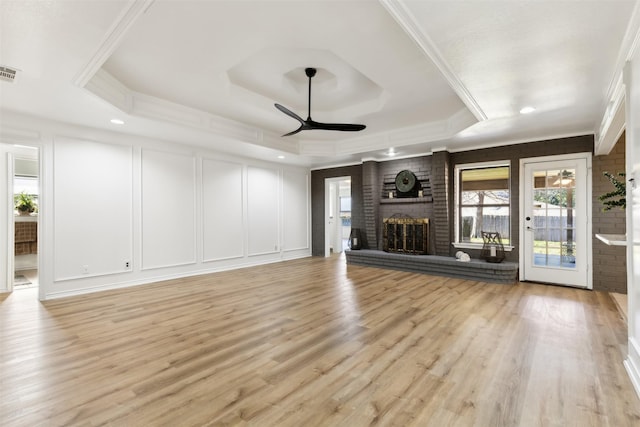 unfurnished living room featuring a brick fireplace, light hardwood / wood-style flooring, a raised ceiling, and ceiling fan