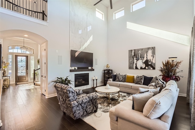 living room featuring dark wood-type flooring, a high ceiling, and a large fireplace