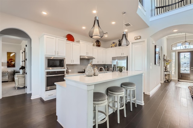 kitchen with white cabinetry, hanging light fixtures, stainless steel appliances, and an island with sink