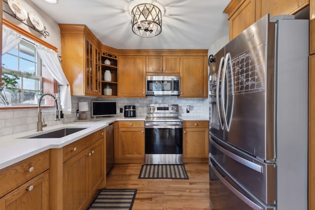 kitchen featuring light hardwood / wood-style flooring, appliances with stainless steel finishes, sink, backsplash, and an inviting chandelier