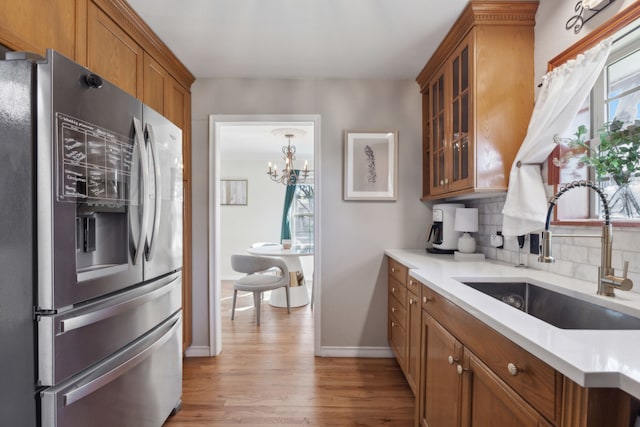 kitchen featuring an inviting chandelier, light hardwood / wood-style floors, sink, tasteful backsplash, and stainless steel fridge with ice dispenser