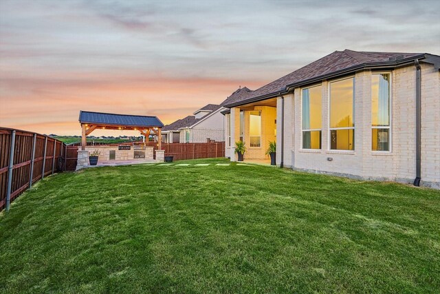 rear view of house featuring a fenced backyard, a yard, brick siding, and a gazebo