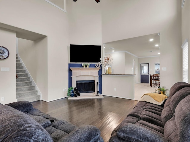 living room featuring a towering ceiling, ceiling fan, ornamental molding, and hardwood / wood-style flooring