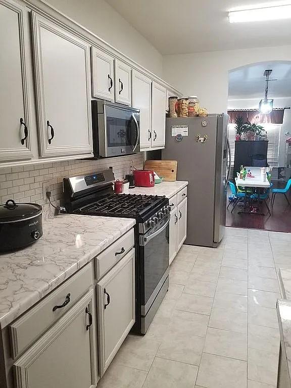 kitchen with hanging light fixtures, light stone counters, backsplash, light tile patterned floors, and appliances with stainless steel finishes