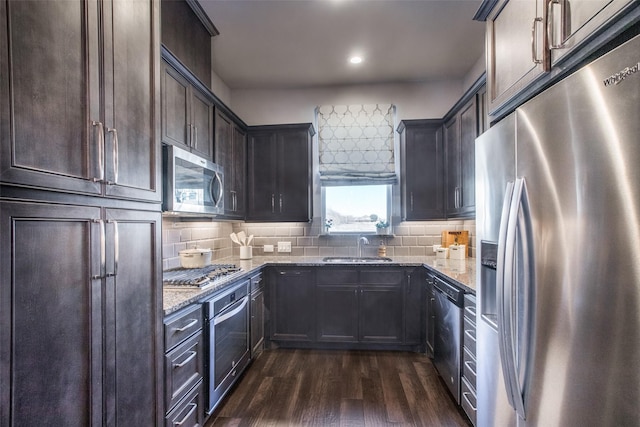 kitchen with dark wood-style floors, tasteful backsplash, appliances with stainless steel finishes, a sink, and light stone countertops