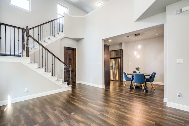 interior space with dark wood-style floors, a high ceiling, stairs, and baseboards