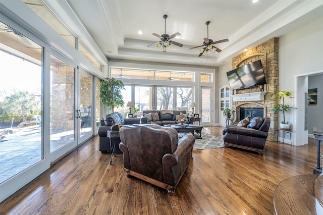 living room with a stone fireplace, a raised ceiling, crown molding, ceiling fan, and dark hardwood / wood-style floors