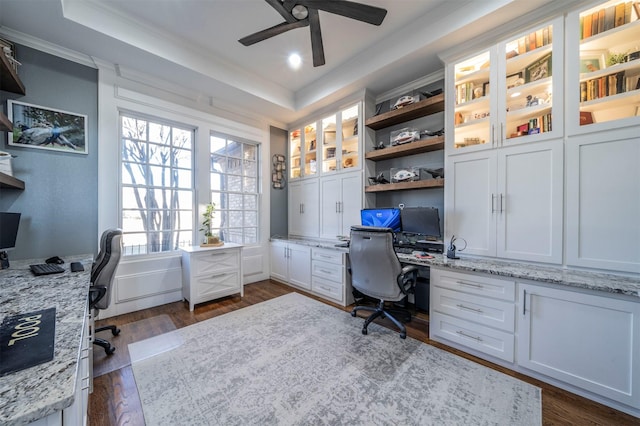 office with dark hardwood / wood-style flooring, ornamental molding, a tray ceiling, ceiling fan, and built in desk