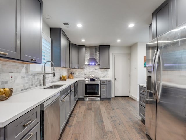 kitchen with gray cabinetry, wall chimney range hood, sink, appliances with stainless steel finishes, and light hardwood / wood-style floors