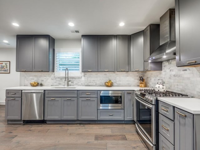 kitchen with stainless steel appliances, gray cabinetry, and wall chimney range hood