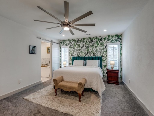 carpeted bedroom featuring a barn door, ensuite bath, and ceiling fan