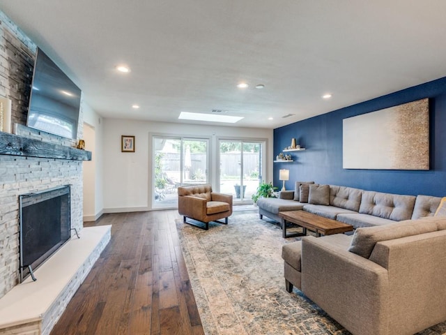 living room featuring hardwood / wood-style floors, a fireplace, and a skylight