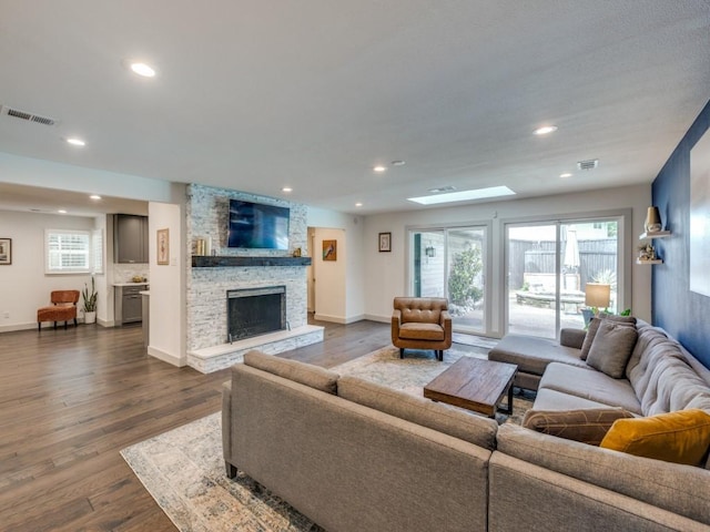 living room featuring dark hardwood / wood-style flooring, a stone fireplace, and a skylight