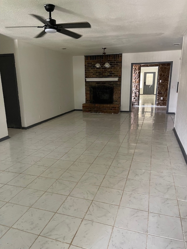 unfurnished living room featuring ceiling fan, a fireplace, brick wall, and a textured ceiling