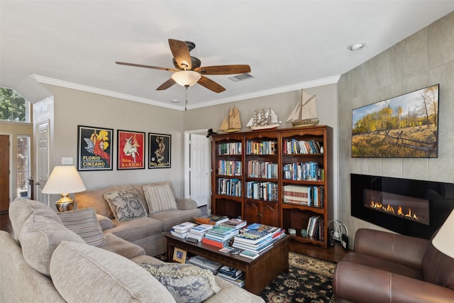 living room featuring wood-type flooring, ceiling fan, crown molding, and a tiled fireplace