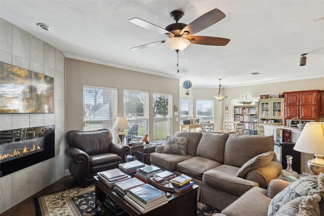 living room with ceiling fan, wood-type flooring, ornamental molding, and a tiled fireplace