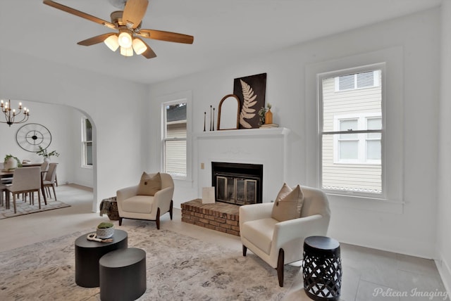 living room with ceiling fan with notable chandelier and a brick fireplace