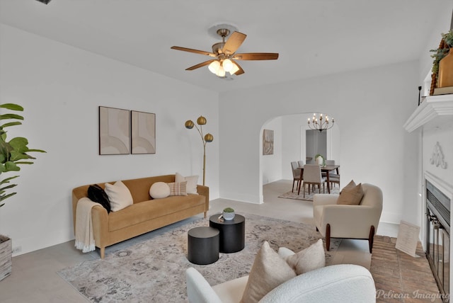 living room with a fireplace, concrete floors, and ceiling fan with notable chandelier