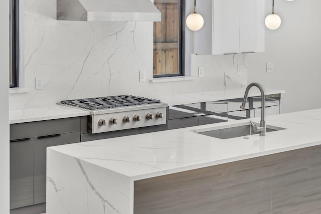 kitchen featuring stainless steel gas stovetop, backsplash, wall chimney range hood, decorative light fixtures, and light stone counters