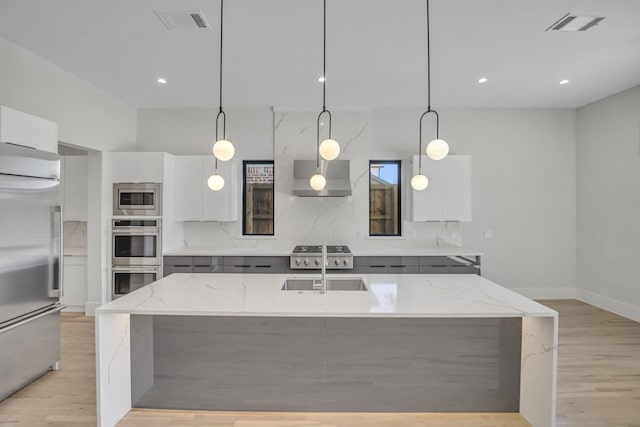 kitchen featuring white cabinetry, light stone counters, built in appliances, decorative light fixtures, and a kitchen island with sink