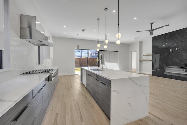 kitchen with light stone countertops, decorative light fixtures, a spacious island, and wall chimney range hood