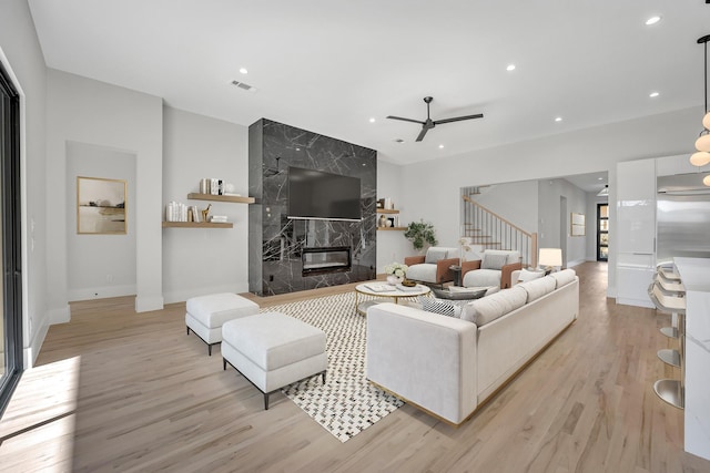 living room with ceiling fan, a high end fireplace, and light hardwood / wood-style floors