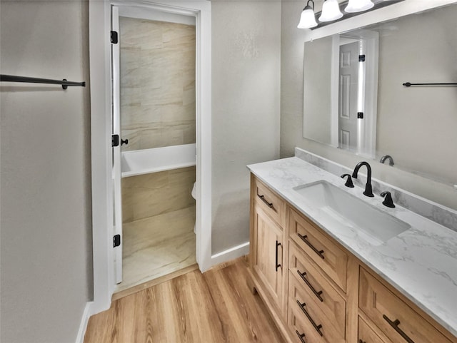 bathroom featuring wood-type flooring, vanity, and a relaxing tiled tub