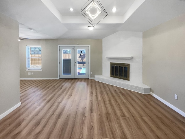 unfurnished living room featuring wood-type flooring, a brick fireplace, french doors, and a raised ceiling