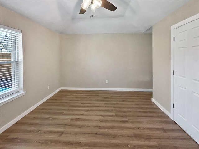 empty room with ceiling fan, a tray ceiling, and dark wood-type flooring