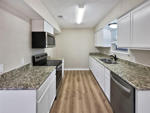 kitchen with light hardwood / wood-style flooring, stainless steel appliances, white cabinets, dark stone counters, and sink