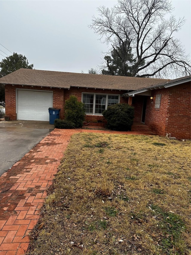 single story home with a garage, a front lawn, brick siding, and driveway