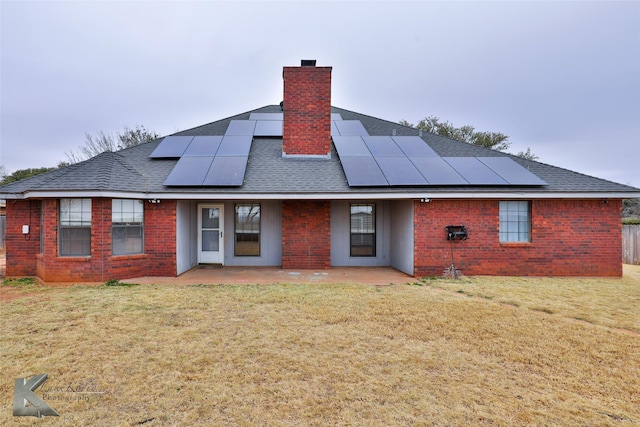 back of property with a yard, a patio area, and solar panels