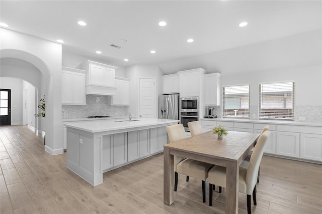 kitchen with a center island with sink, white cabinets, stainless steel appliances, and light hardwood / wood-style flooring