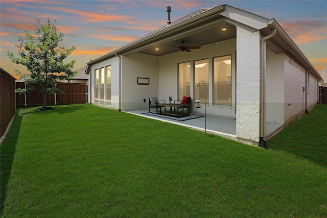 back house at dusk with a lawn, ceiling fan, and a patio