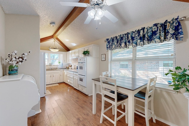 kitchen featuring white cabinetry, ceiling fan, a kitchen breakfast bar, light hardwood / wood-style flooring, and lofted ceiling with beams