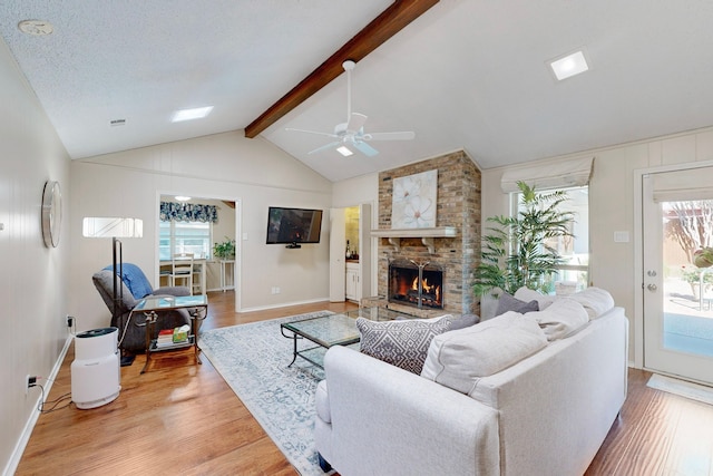 living room featuring a textured ceiling, ceiling fan, vaulted ceiling with beams, light hardwood / wood-style floors, and a stone fireplace