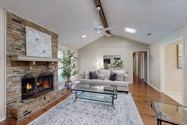 living room with ceiling fan, a brick fireplace, vaulted ceiling with beams, wood-type flooring, and a textured ceiling