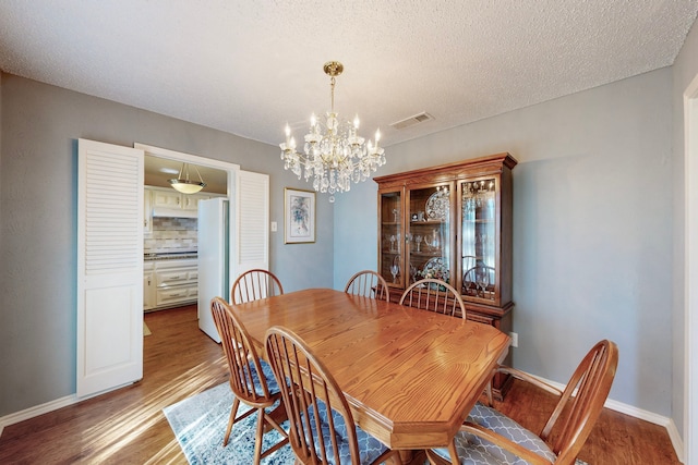 dining room featuring light wood-type flooring, a textured ceiling, and an inviting chandelier