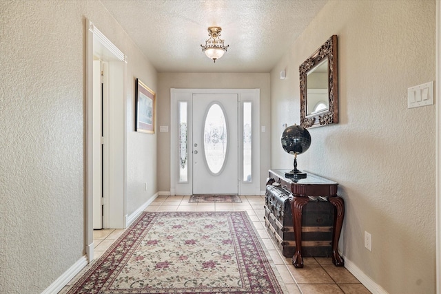 foyer entrance featuring light tile patterned floors, a textured wall, a textured ceiling, and baseboards