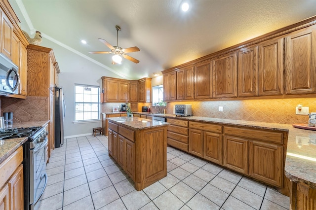 kitchen with stainless steel appliances, brown cabinets, vaulted ceiling, a ceiling fan, and tasteful backsplash