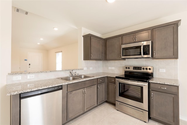 kitchen featuring kitchen peninsula, appliances with stainless steel finishes, light stone counters, and sink