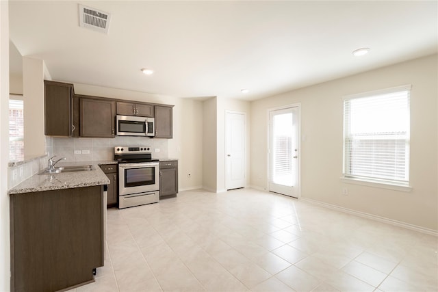 kitchen featuring dark brown cabinetry, light stone countertops, sink, light tile patterned floors, and appliances with stainless steel finishes