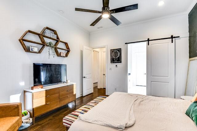 bedroom with a barn door, ceiling fan, crown molding, and dark hardwood / wood-style floors