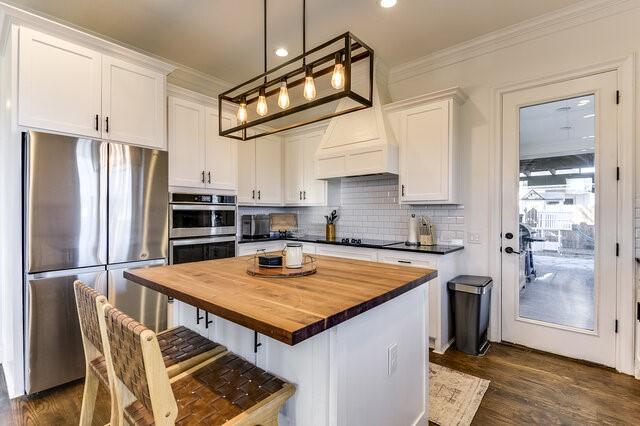 kitchen featuring a center island, white cabinets, appliances with stainless steel finishes, butcher block countertops, and decorative light fixtures