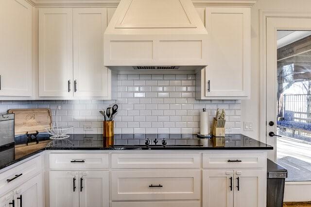 kitchen with decorative backsplash, white cabinets, dark stone counters, and custom range hood