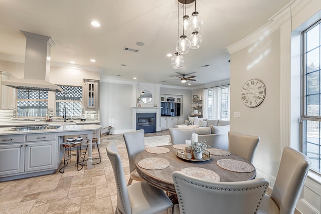 dining space with sink, crown molding, a fireplace, and ceiling fan