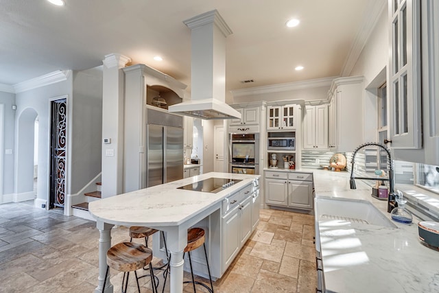 kitchen with sink, built in appliances, island exhaust hood, light stone countertops, and white cabinets