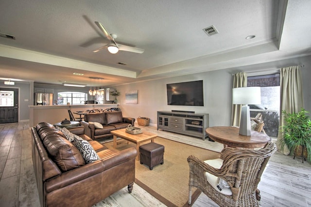 living room featuring ornamental molding, a textured ceiling, a tray ceiling, ceiling fan, and light hardwood / wood-style flooring