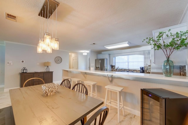 dining room with a textured ceiling, light hardwood / wood-style floors, wine cooler, and ornamental molding