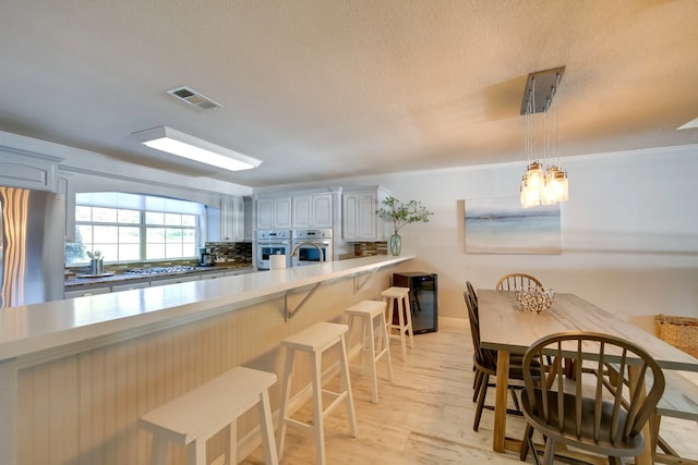 kitchen with a kitchen breakfast bar, backsplash, a textured ceiling, decorative light fixtures, and gray cabinets